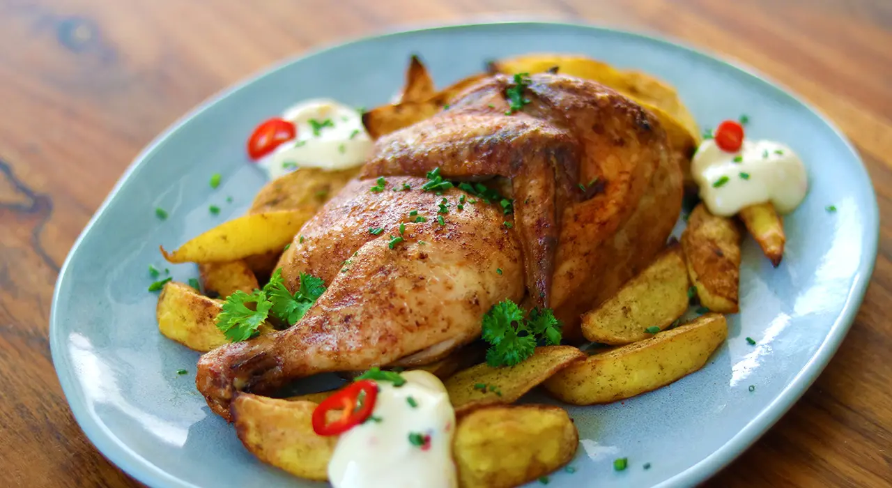 halbes Hähnchen liegend auf Kartoffel Wedges auf blauem Teller